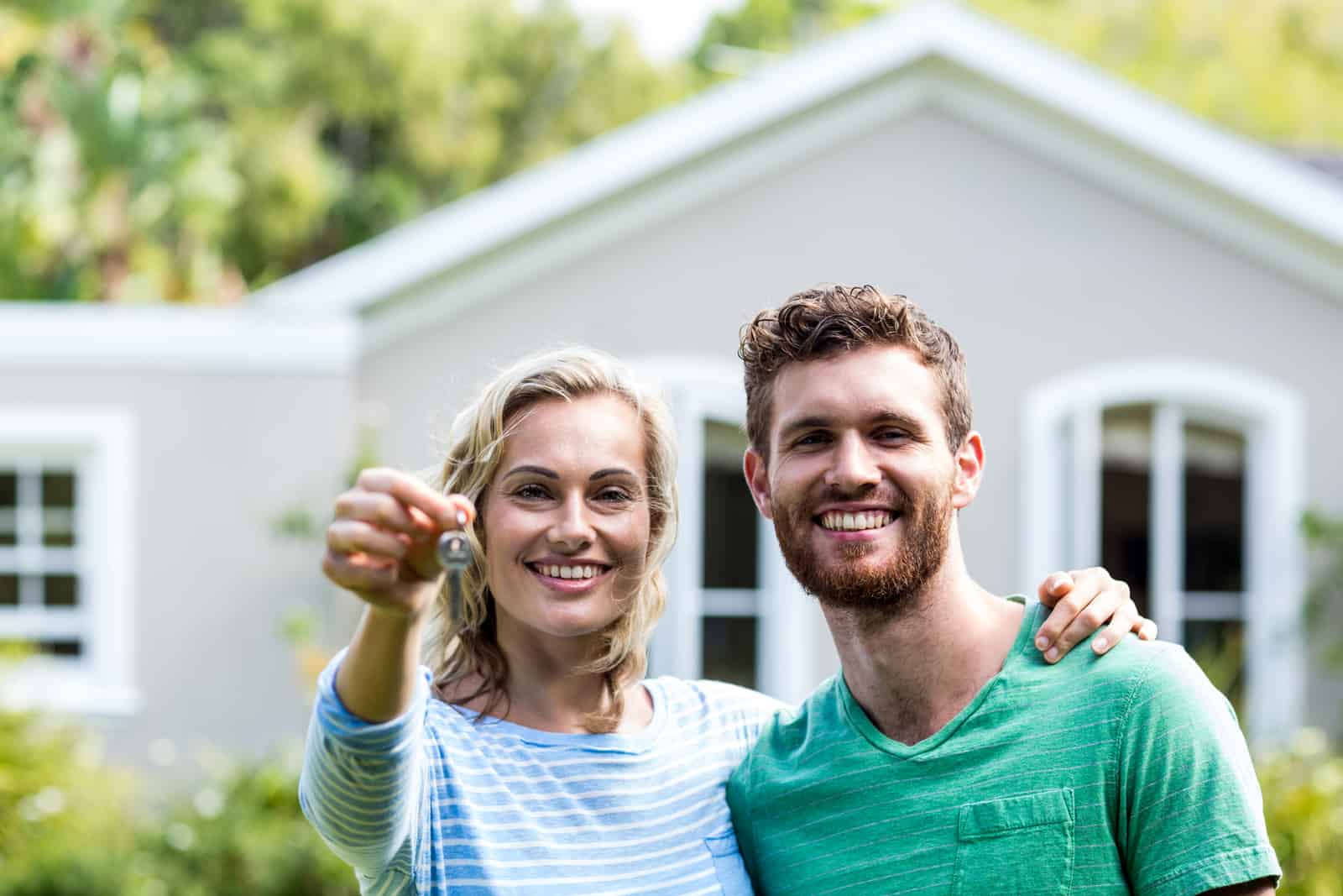 couple-with-keys-standing-against-house